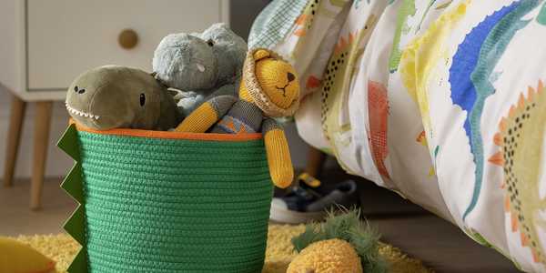 A dino rope basket in green and orange with stuffed toys in it.